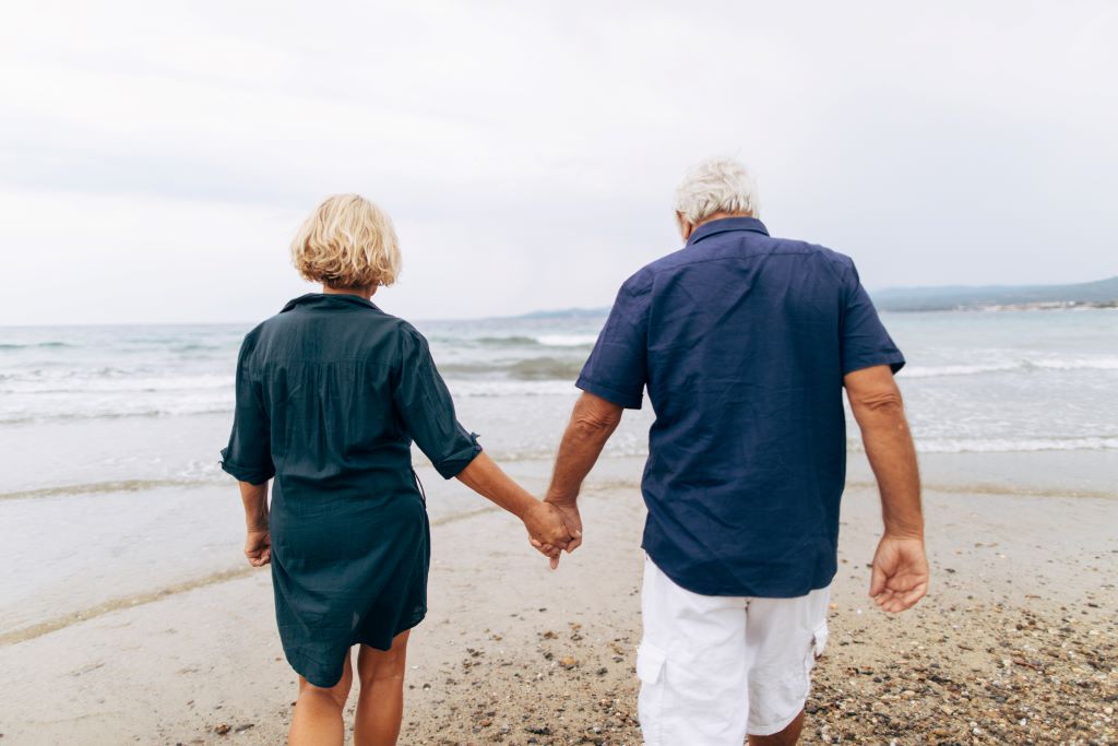 Midaldrende kvinde og mand går hånd i hånd med hinanden en tur langs stranden