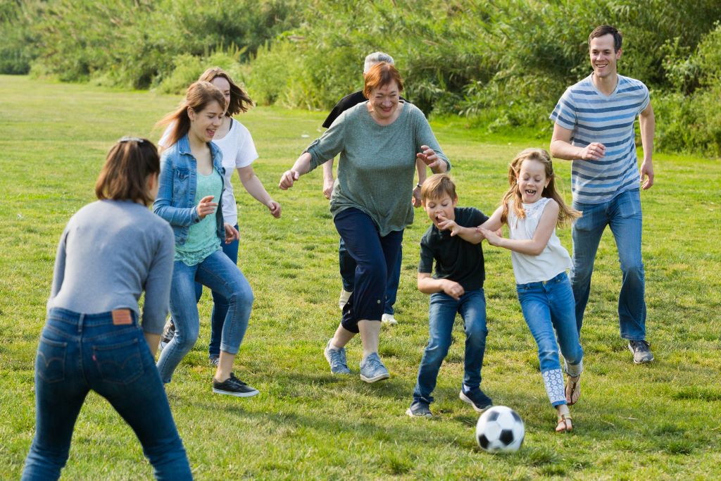muntre kvinder og mænd spiller fodbold med børn på en græsplæne